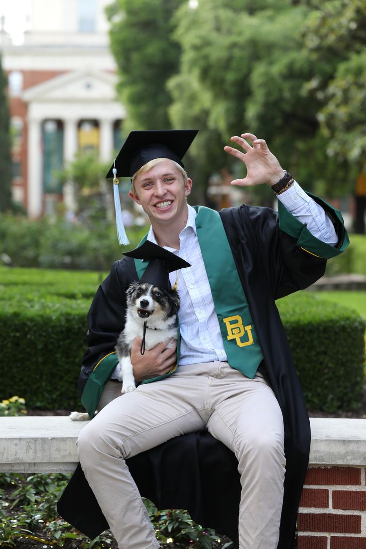 a man in graduation cap and gown sitting on a bench with his dog, waving