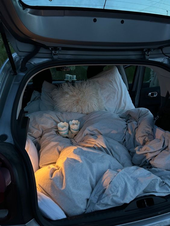 an open hatchback car trunk with pillows and blankets in the bed area at night