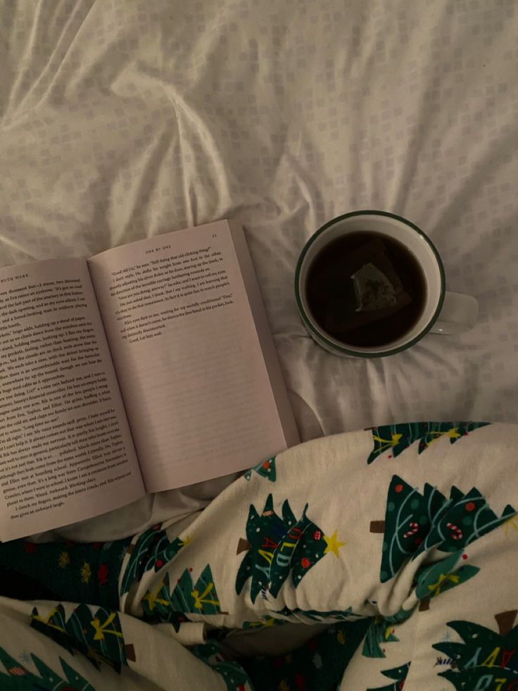 an open book sitting on top of a bed next to a cup of coffee and pillow