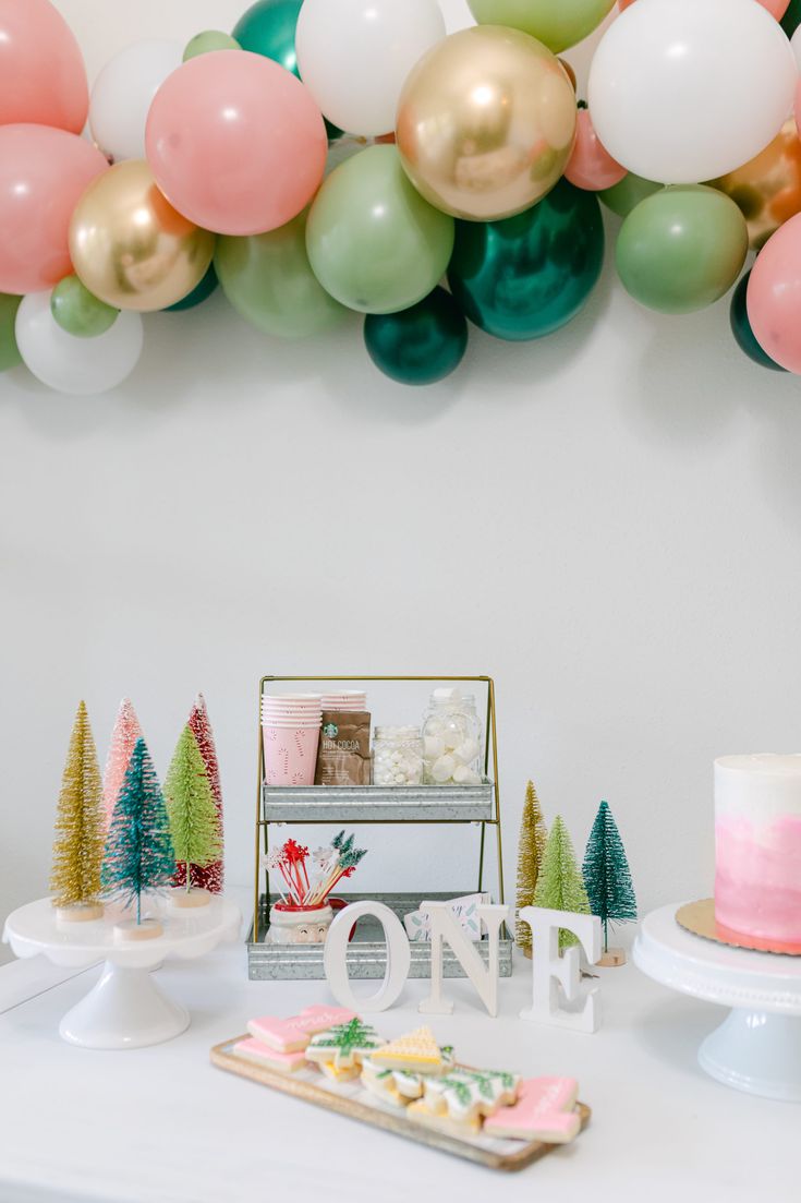 a table topped with cake and balloons next to a sign that says one on it