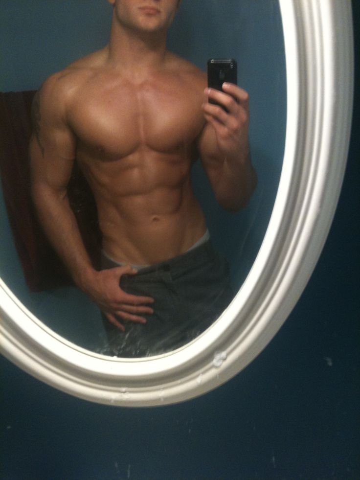 a shirtless man taking a selfie in front of a round mirror with his cell phone