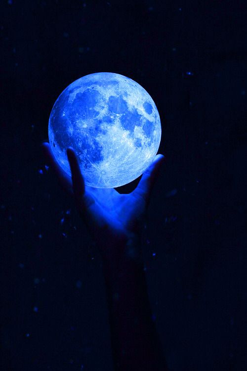 a person's hand holding a glowing blue moon in the dark