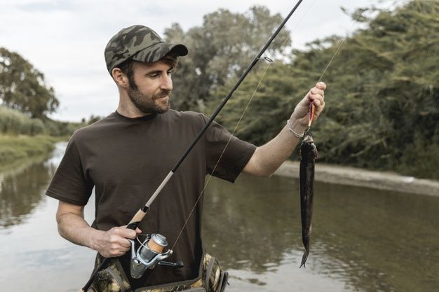 a man standing in the water holding a fishing rod and a fish caught on a line