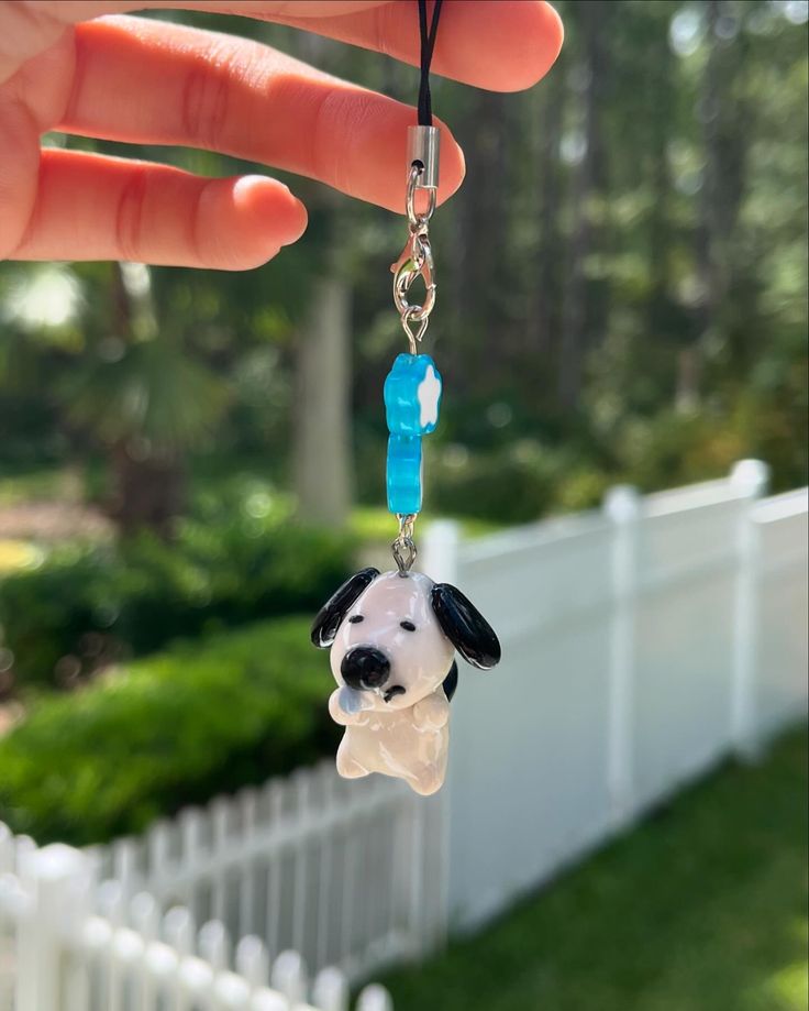 a hand holding a key chain with a small dog on it's face and a blue bead around the neck