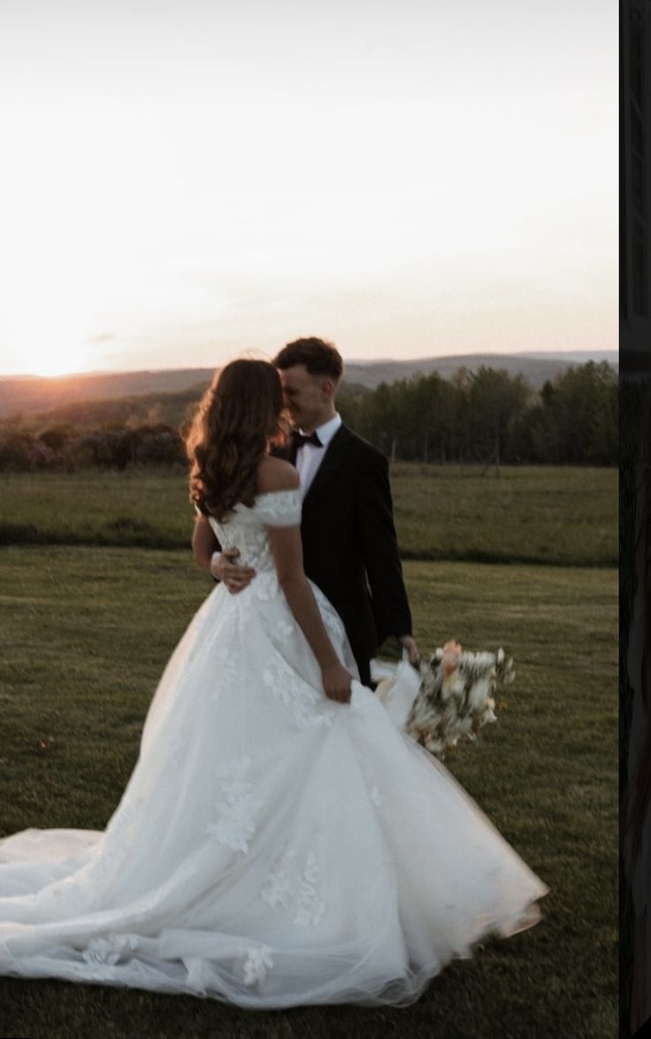 a bride and groom standing in the grass at sunset