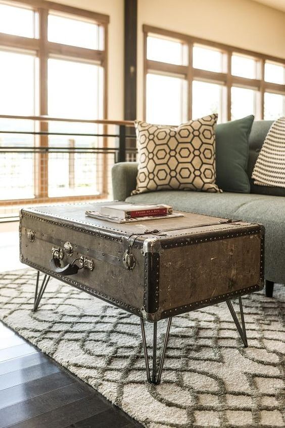 an old trunk is sitting on the floor in front of a gray couch with black and white pillows