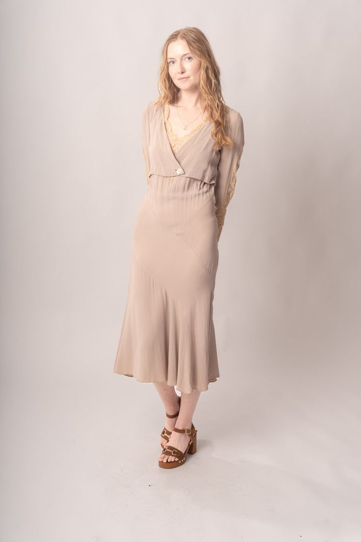 Stunningly preserved 1920’s mauve & ecru bias cut dress with attached jacket, lace trim, and asymmetrical cut. Best fits modern size S-M Length 52”Pit to pit 18.5”Waist 26-30”Hips 31-42” Model’s Measurements:Height 5’9”Chest 34”Waist 29”Hips 36.5” Excellent vintage condition, with normal wear and condition for its age.For international shipping rates, please send inquiries to our CONTACT page. Taupe Fitted V-neck Dress, Fitted Feminine Rayon Midi Dress, Fitted Knee-length Taupe Dress, Fitted Taupe Knee-length Dress, Taupe Fitted Knee-length Dress, Fitted Vintage V-neck Dress For Daywear, Fitted V-neck Vintage Dress For Daywear, Fitted Taupe V-neck Dress, Fitted Beige Vintage Midi Dress