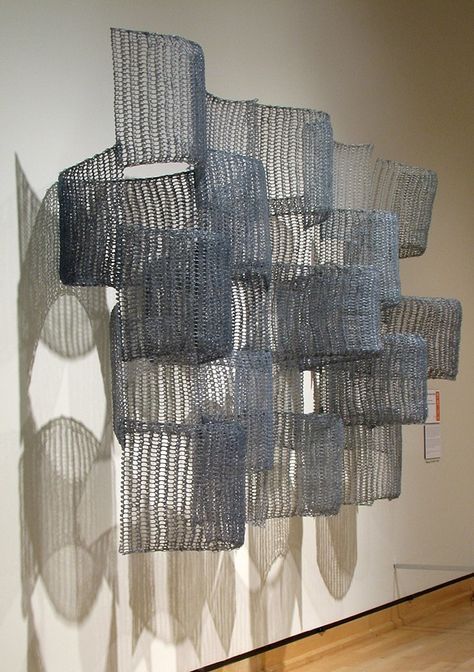 a sculpture made out of wire hanging from the side of a wall next to a wooden floor