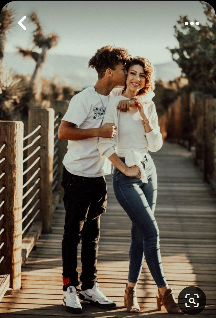 a man and woman standing on a wooden bridge with their arms around each other as they kiss