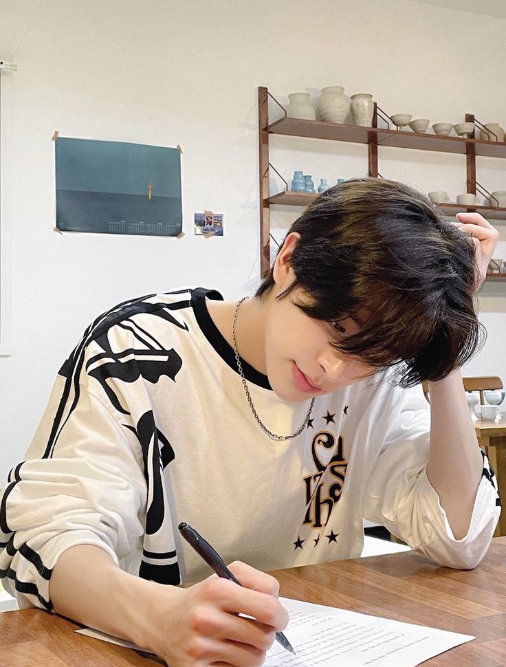 a young man sitting at a table writing on a piece of paper with a pen in his hand