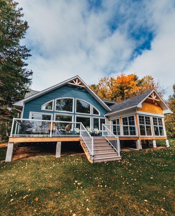 a blue house sitting on top of a lush green hillside next to trees and grass