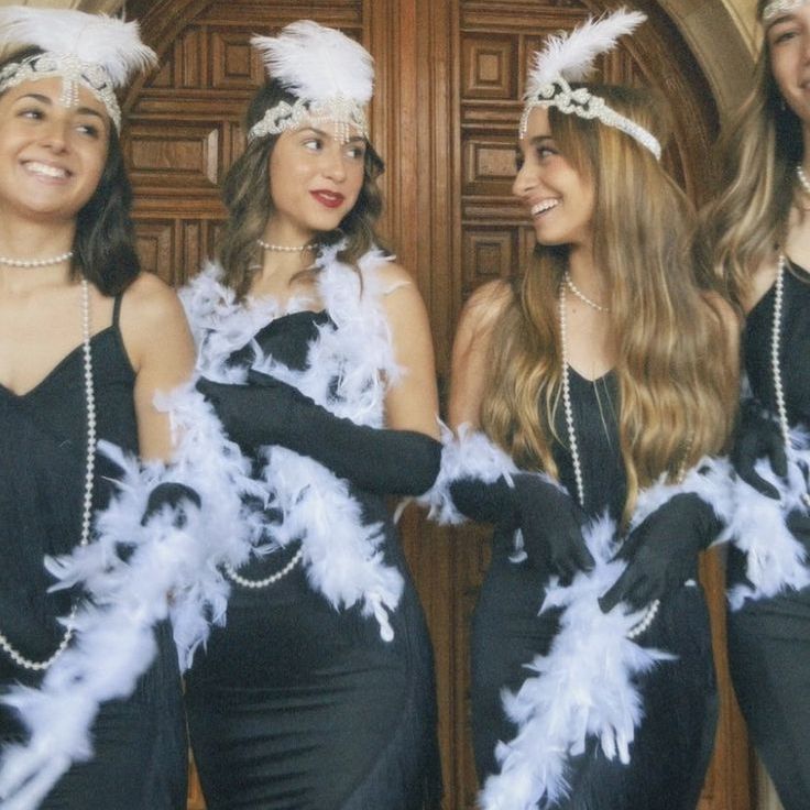 three women dressed in black and white posing for the camera with feathers on their head