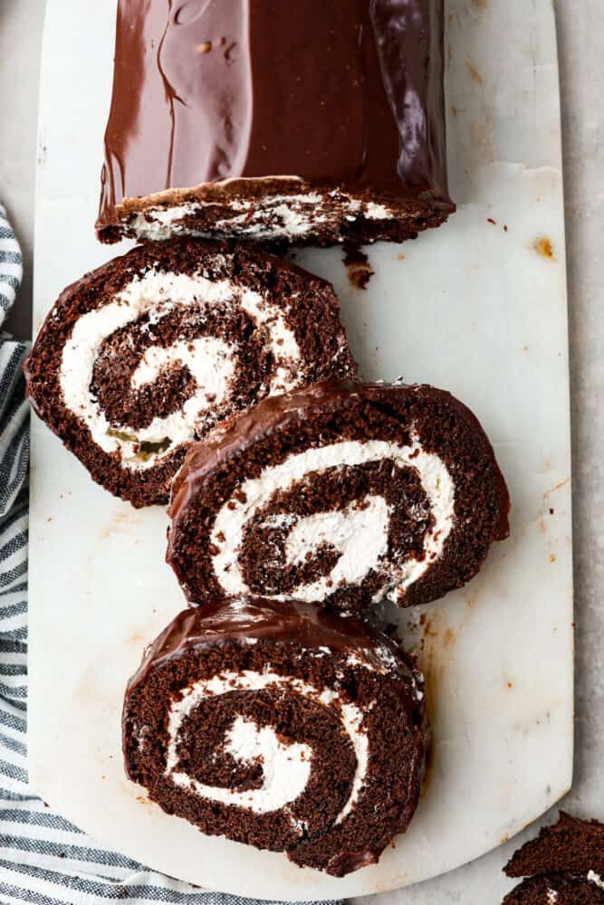 chocolate roll with white frosting sitting on top of a cutting board next to sliced cake