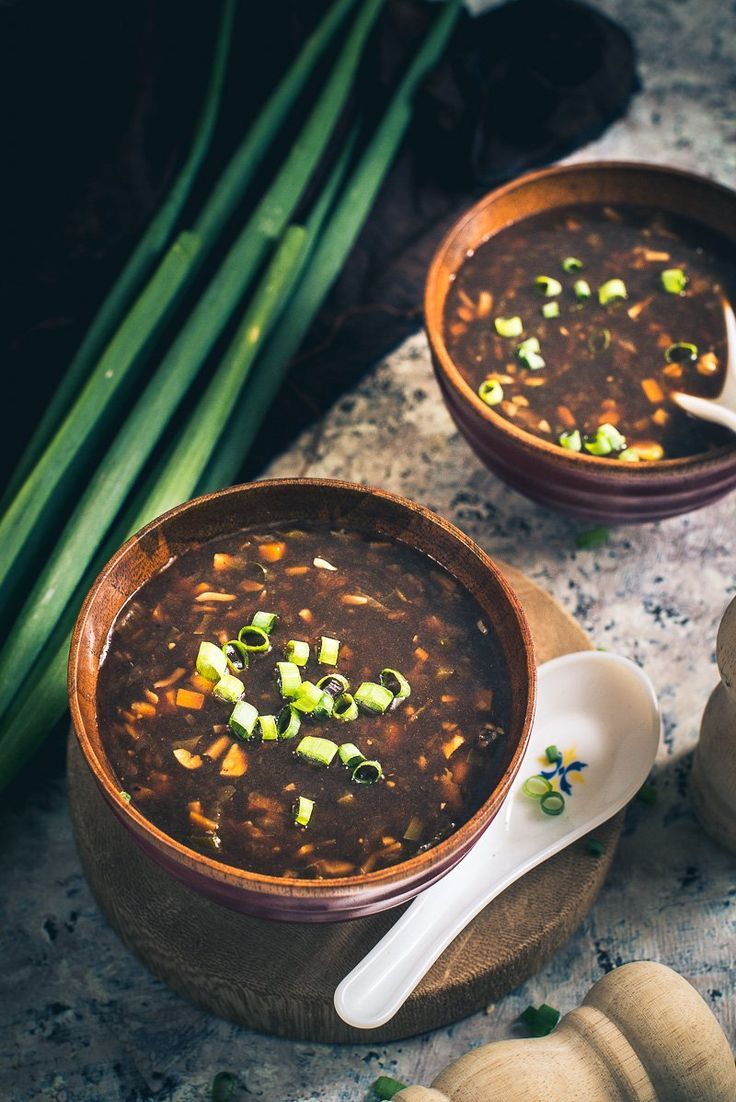 two bowls filled with soup sitting on top of a table next to garlic and green onions