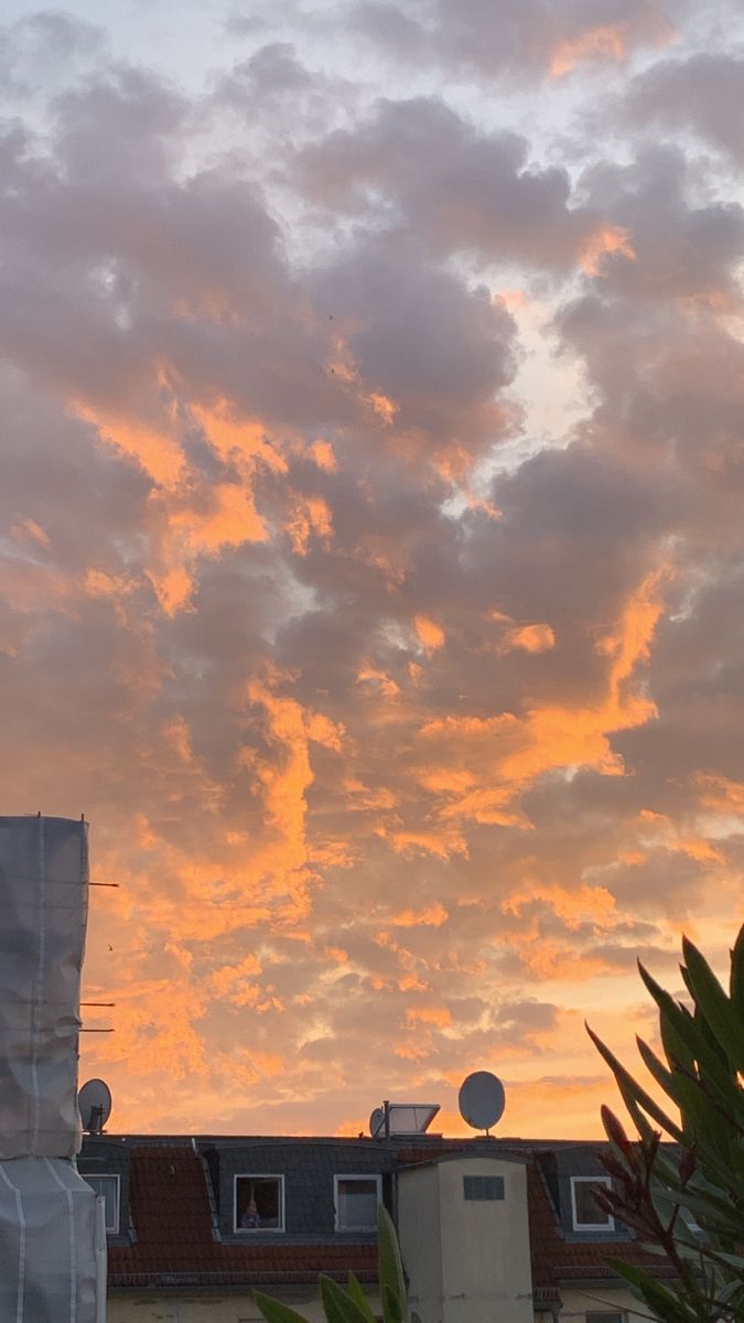 the sun is setting behind some clouds in the sky above buildings and trees with no leaves on them