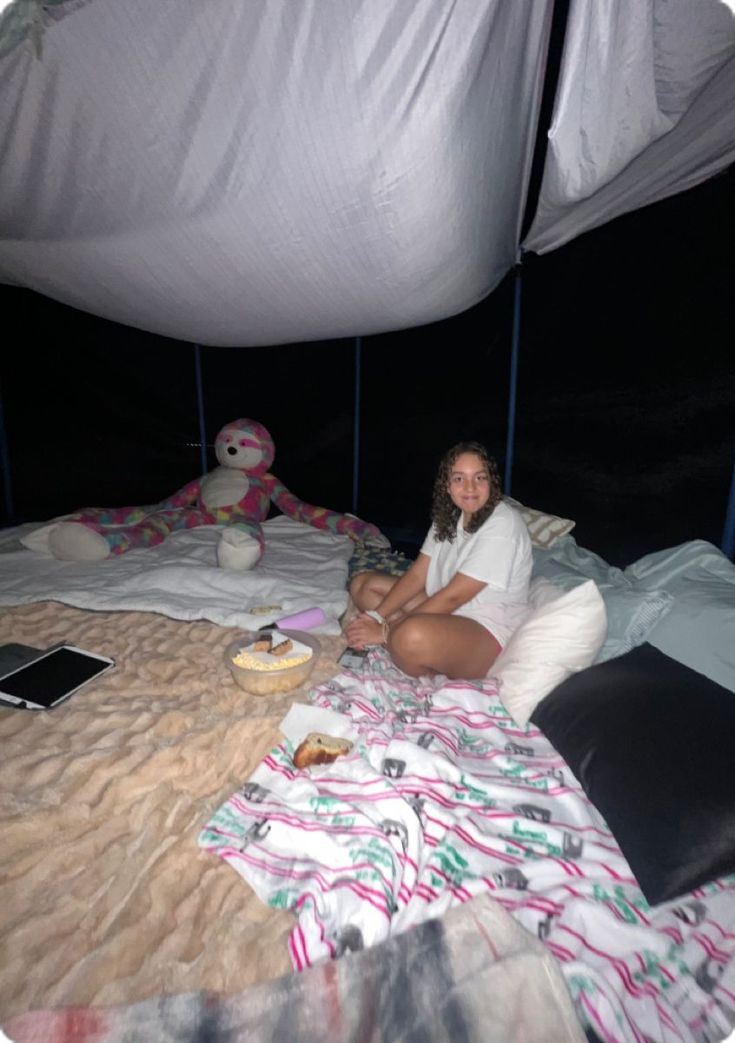 a woman sitting on top of a bed next to a stuffed animal in a tent