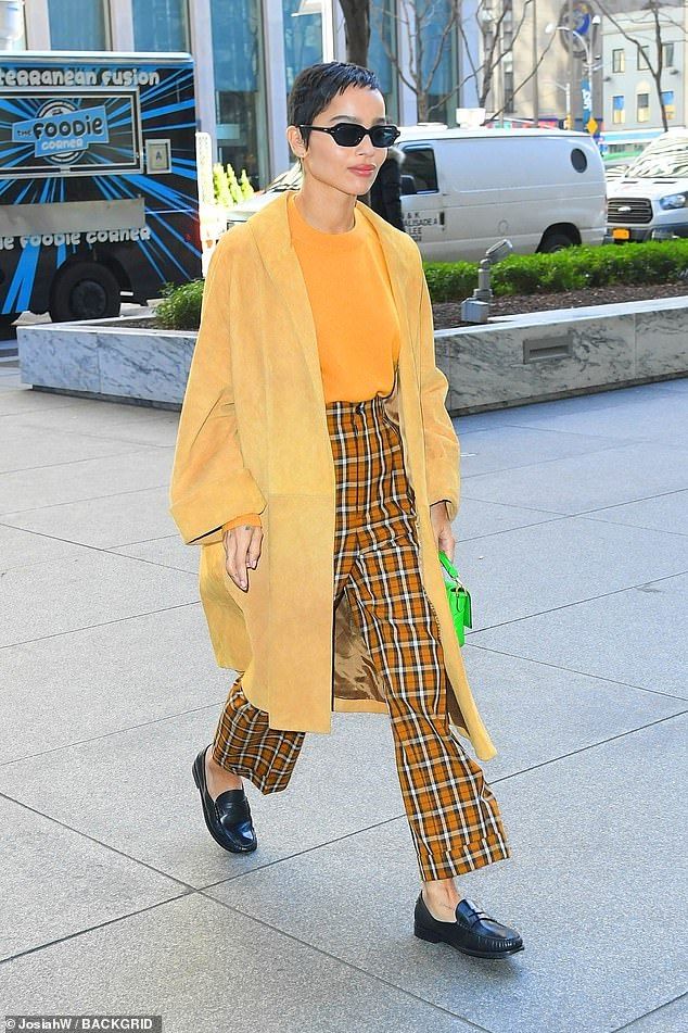 a woman in yellow coat and plaid pants walking down the street with her hand on her hip