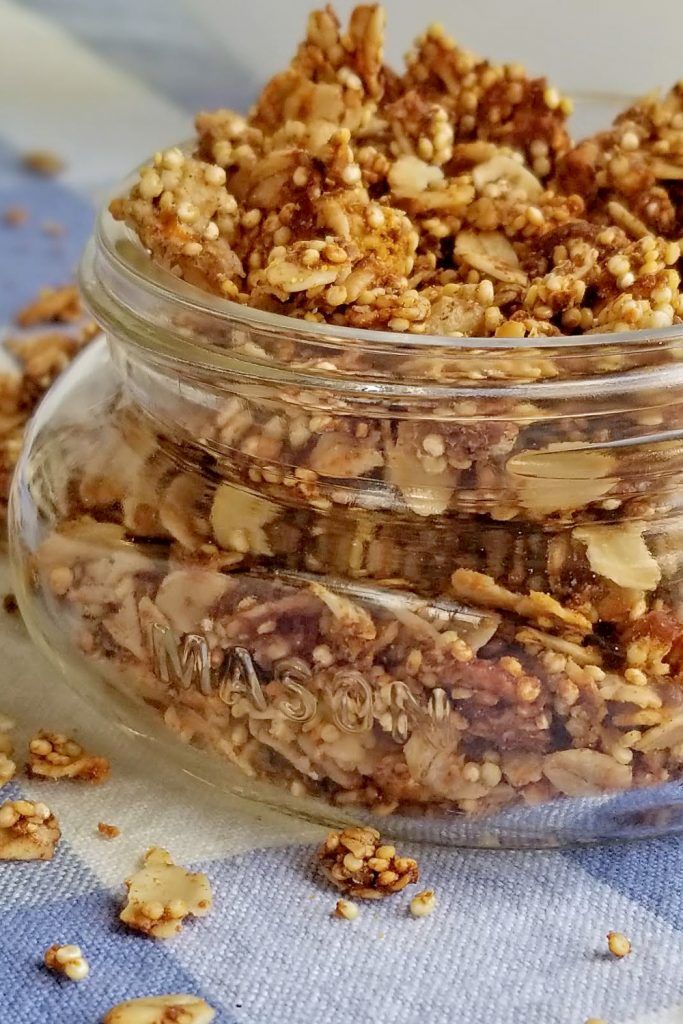 granola in a glass jar sitting on a blue and white table cloth next to some nuts