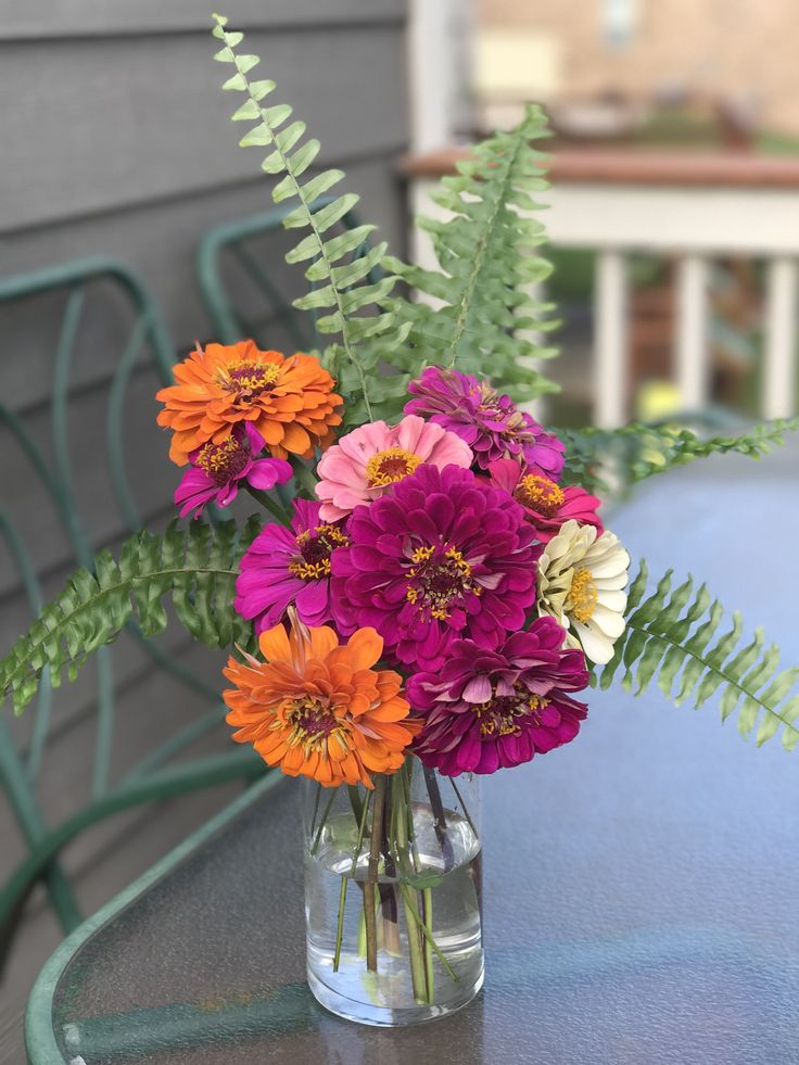 a vase filled with colorful flowers sitting on top of a table next to a green chair