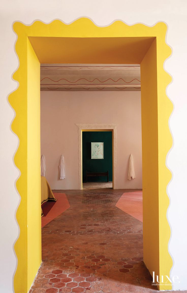 an open doorway in a room with red brick floors and white walls, leading to a painting on the wall