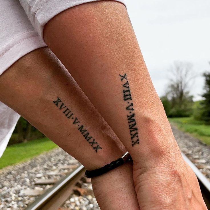 two people with matching tattoos on their arms holding each other's hands while standing next to train tracks