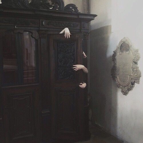 an arm reaching out from behind a wooden cabinet