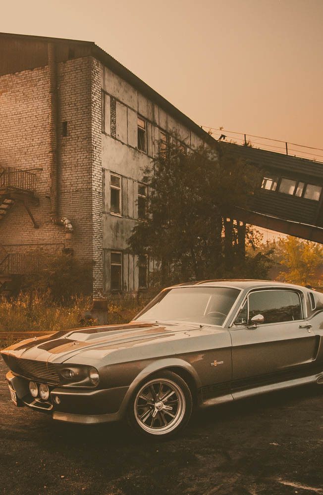 an old muscle car parked in front of a run down building