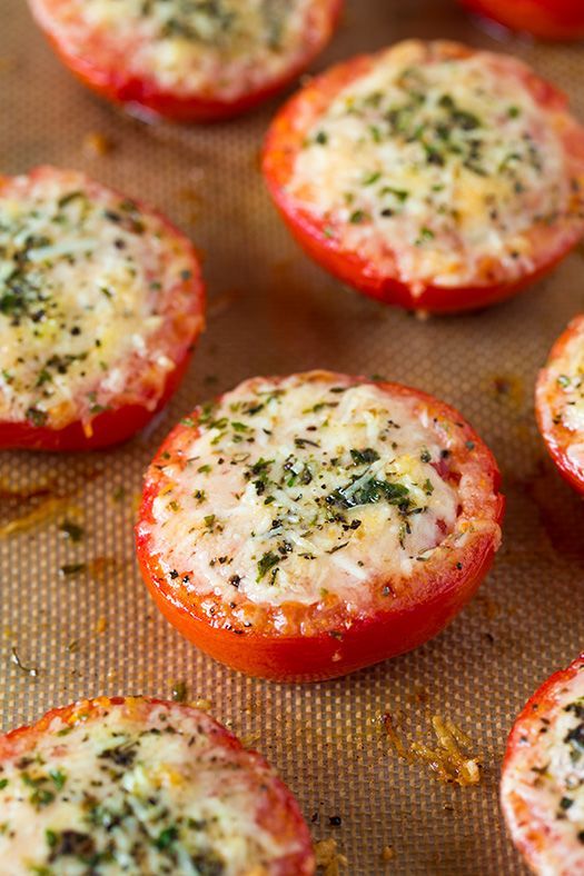 tomatoes with cheese and herbs on them sitting on a baking sheet