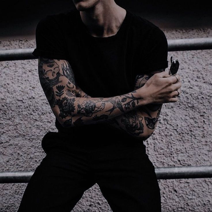 a man with tattoos sitting on a bench holding his arms crossed and looking at the camera