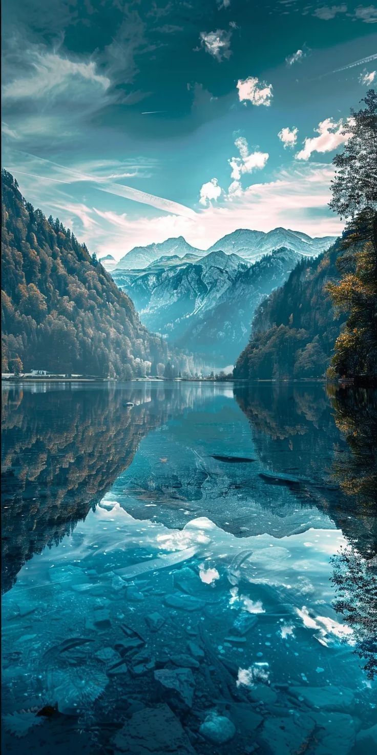 a lake surrounded by mountains and trees under a cloudy blue sky with clouds in the distance