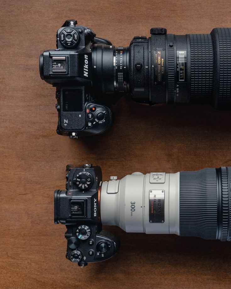 two cameras sitting next to each other on top of a wooden table