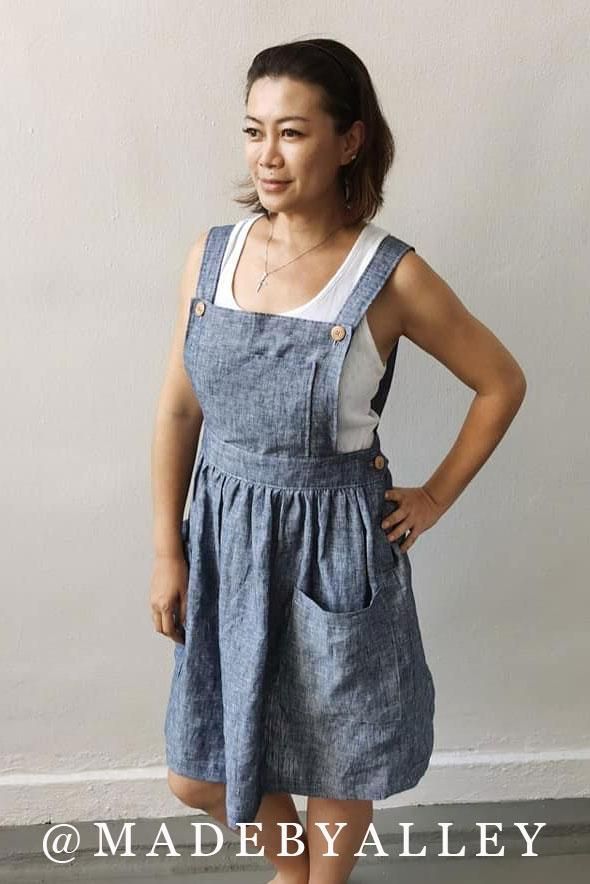 a woman standing in front of a white wall wearing a blue dress with buttons on it