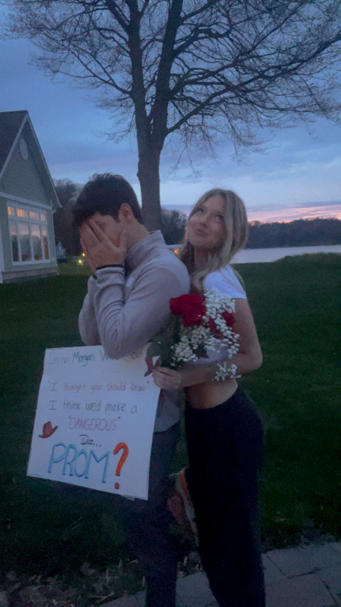 a man and woman standing in front of a house holding a sign that says prom