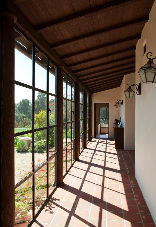 the sun is shining through the windows on the outside of this house, which has long red tile flooring and white walls