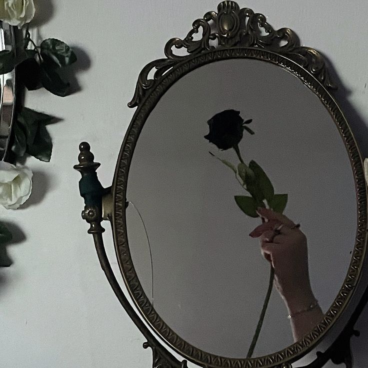 a person holding a flower in front of a mirror with the reflection of a rose on it