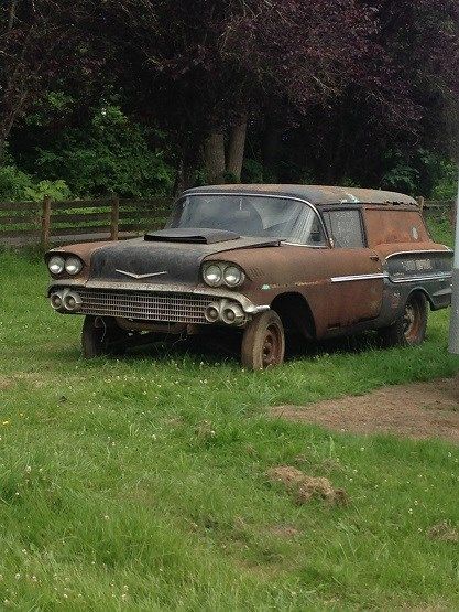 an old car parked in the grass next to a street sign and fenced in area