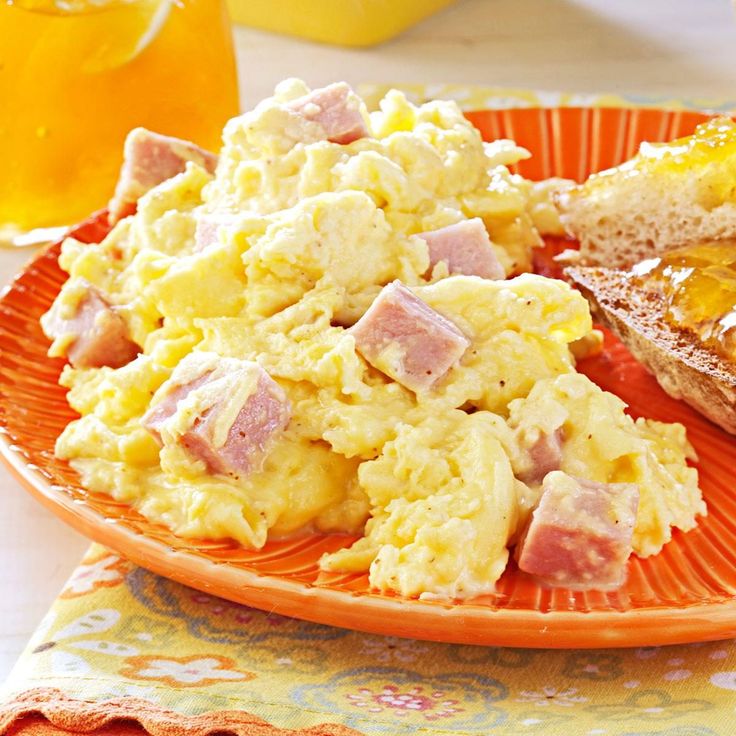 an orange plate topped with mashed potatoes and ham next to a glass of orange juice