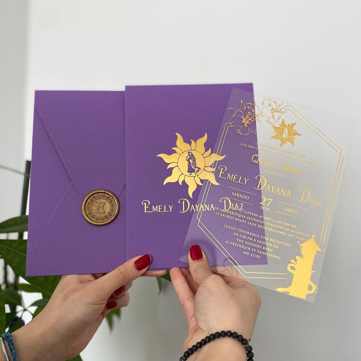 a woman holding up two purple and gold wedding cards