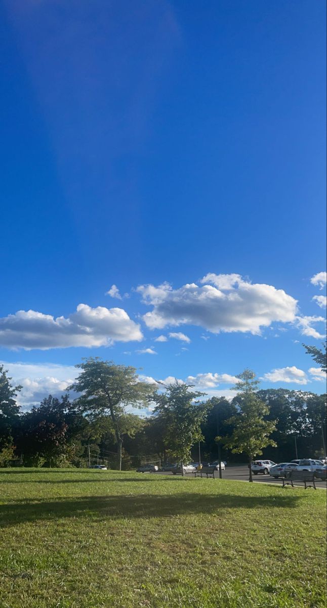 an empty park with cars parked on the grass and clouds in the sky above it