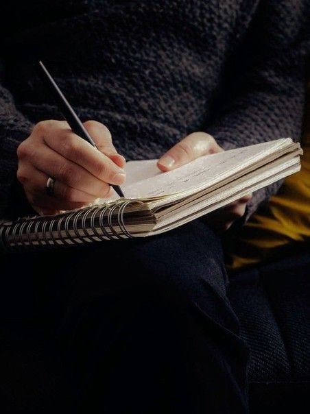 a person holding a pen and writing on a book with an open notebook in front of them