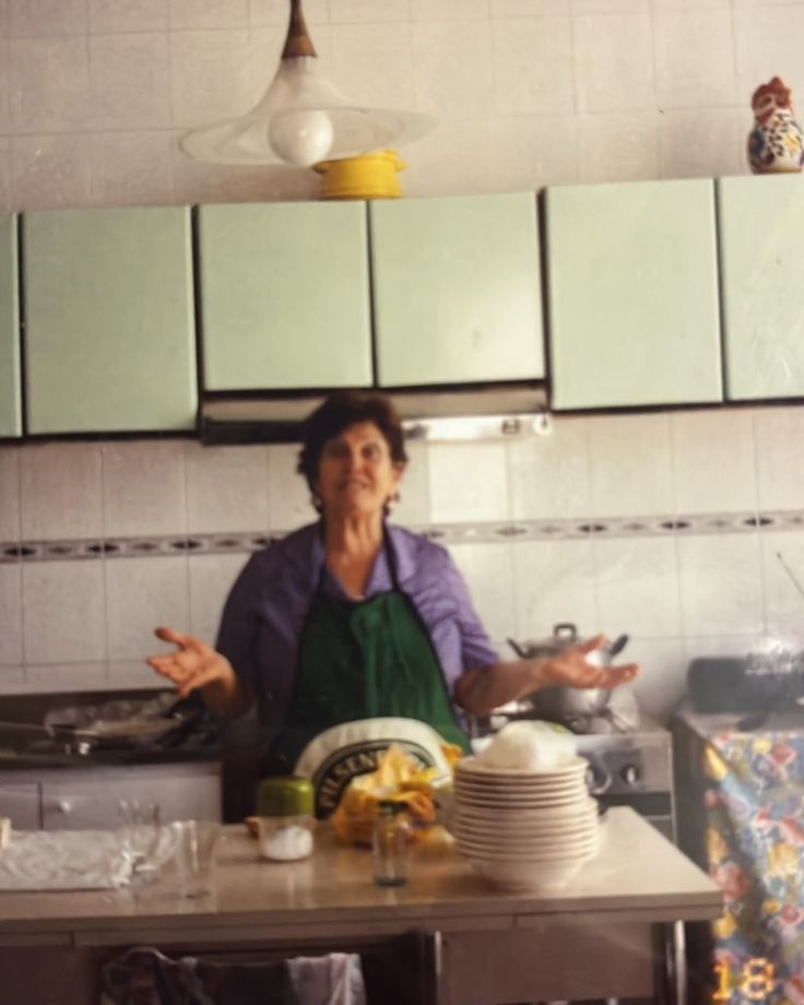 a woman standing in a kitchen with plates and bowls on the counter next to her