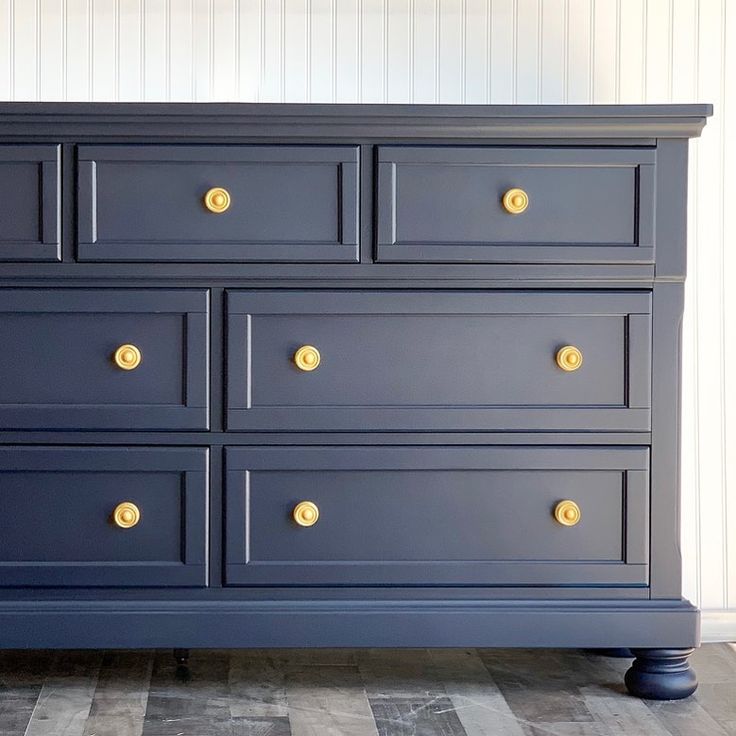 a blue dresser with gold knobs on the top and bottom drawers, against a white wall