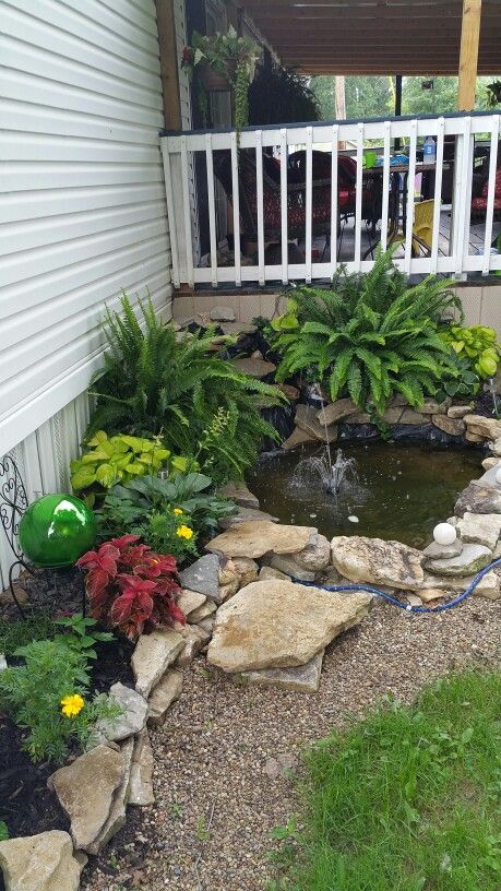 a small pond in the middle of a garden with rocks and plants around it, next to a white fence