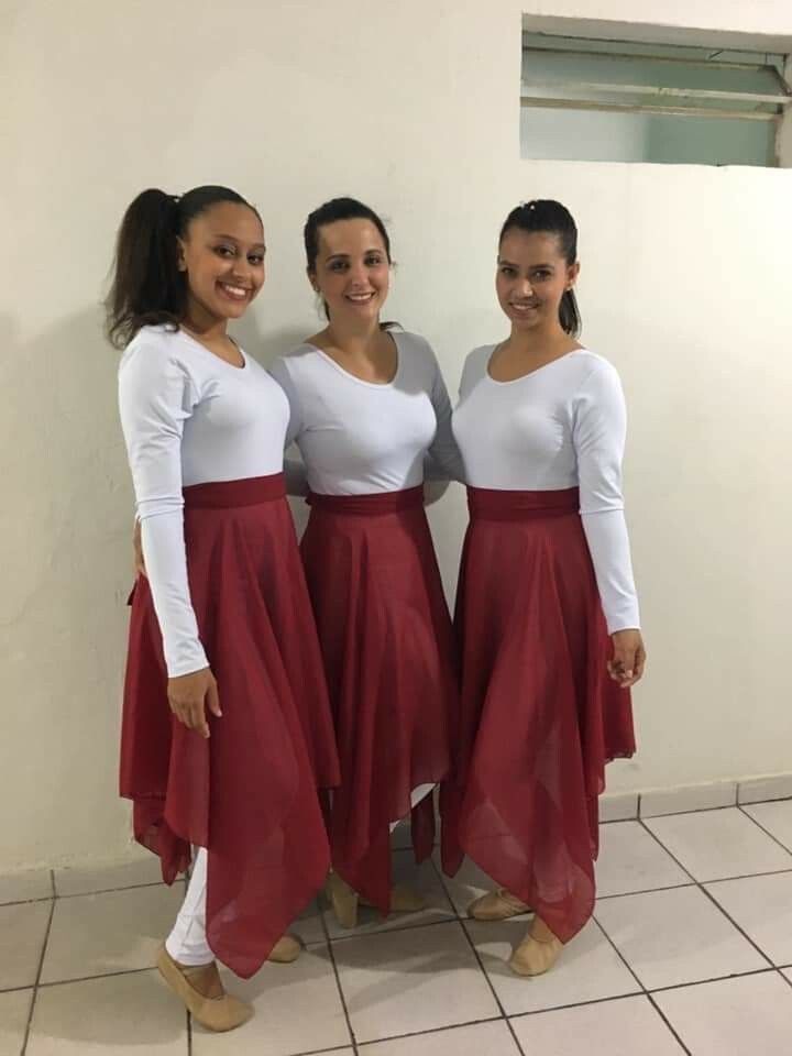 three women standing next to each other wearing long red skirts and white tops, smiling at the camera