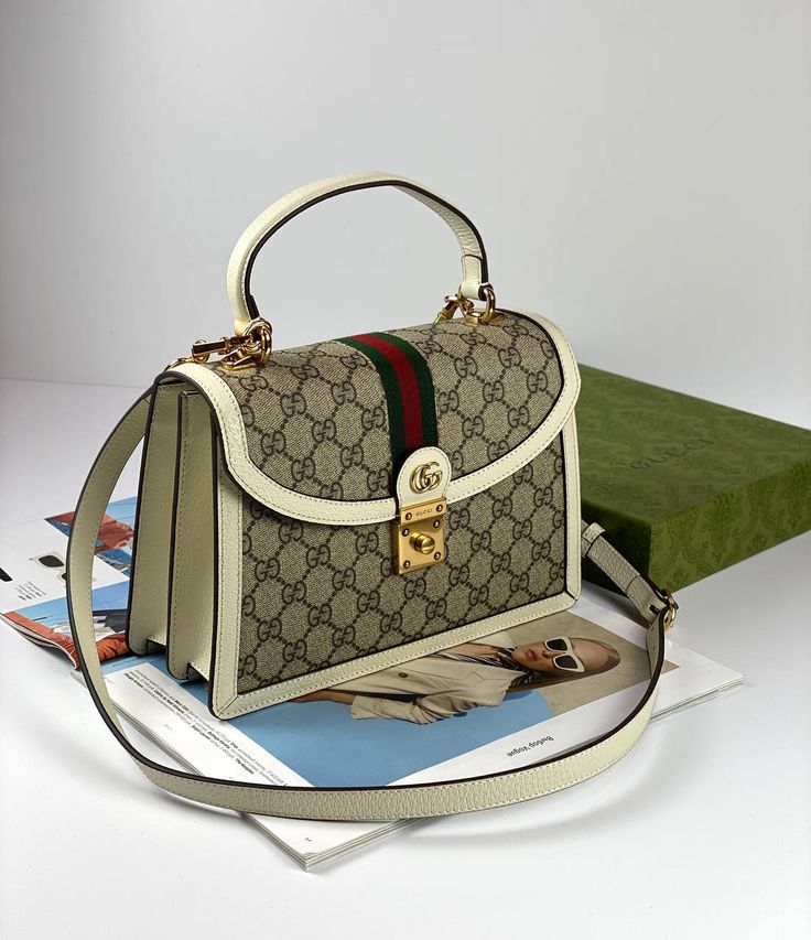 Within Gucci Aria the world of Ophidia evolves with new iterations, combining vintage inspired details with emblematic House codes. This top handle bag is crafted from beige and ebony GG Supreme Canvas, with a distinctive white leather trim and detachable shoulder strap. The inlaid blue and red Web stripe completes the style, a homage to Gucci's equestrian heritage. Gucci Aria, Small Top Handle Bag, Red Web, Clubbing Outfits, Gucci Bags, Vuitton Bag, Bags Designer Fashion, Exclusive Bag, Handle Bag