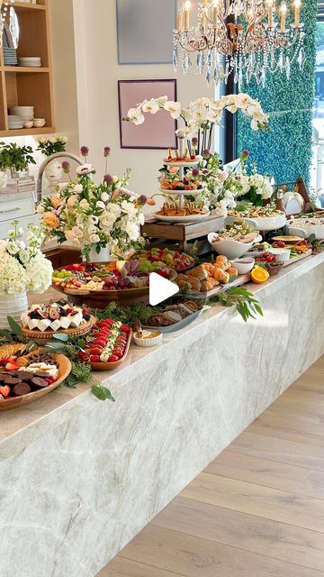 a buffet table filled with lots of food on top of a wooden floor next to a chandelier