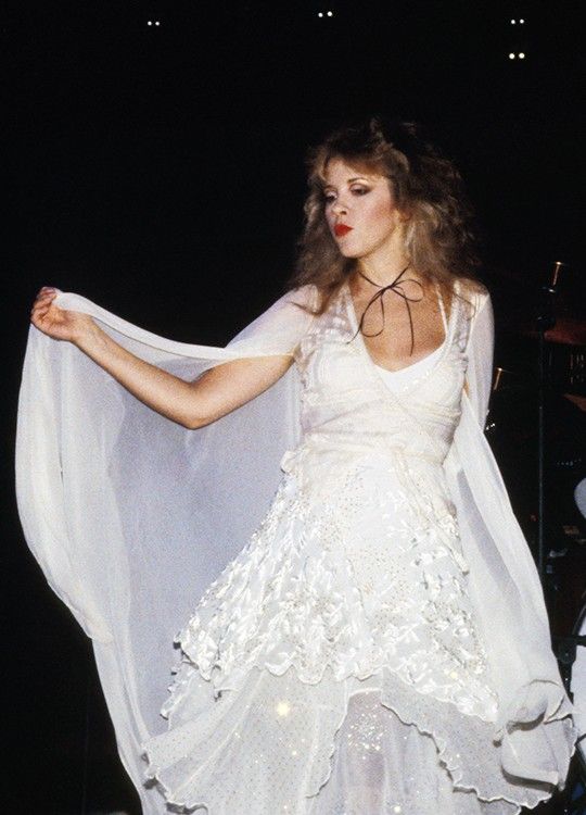 a woman in a white dress and veil on stage with her hands out to the side