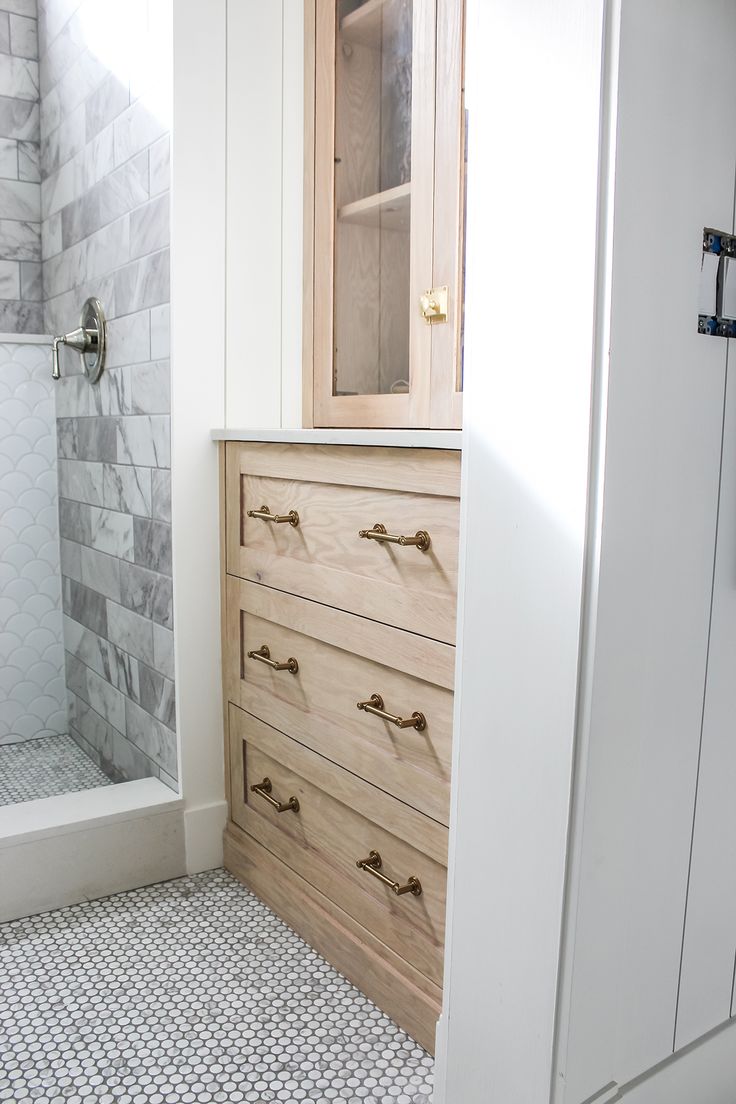 a bathroom with white tile and wooden cabinet in the corner, next to a walk - in shower