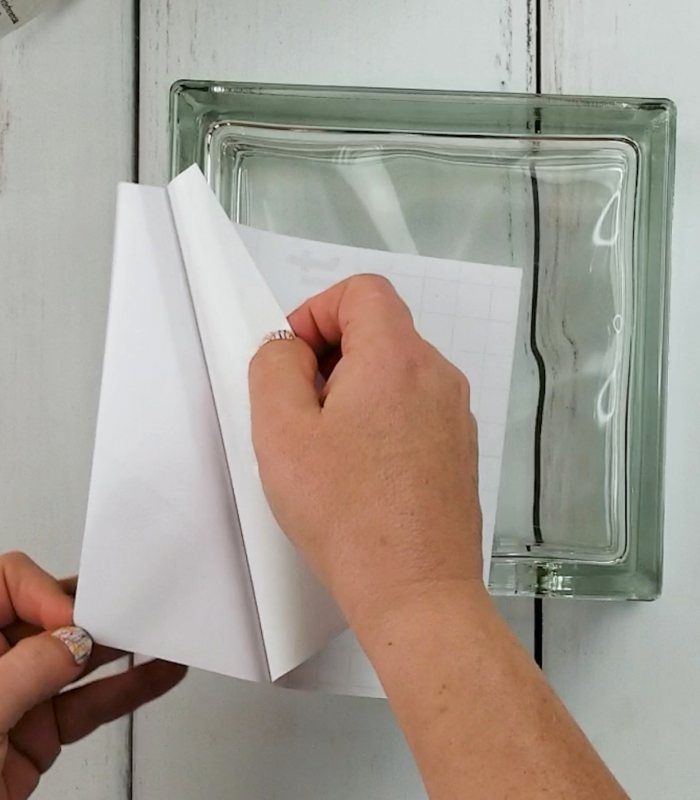 a person is holding an origami piece in front of a glass block on the wall