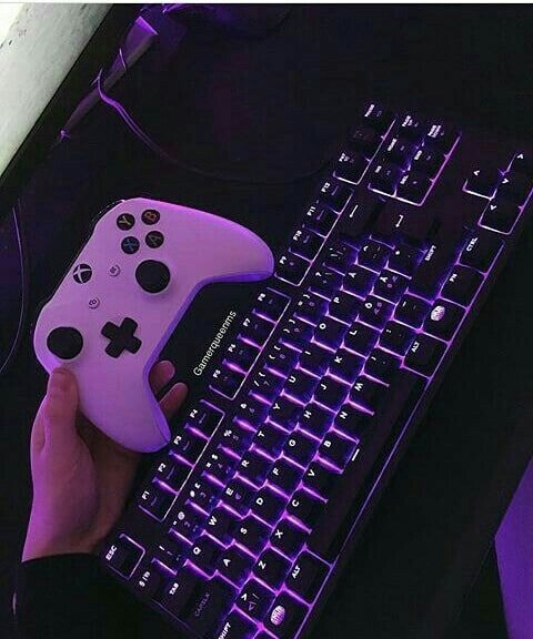 a person holding a game controller next to a keyboard with purple light on it and the key board is lit up